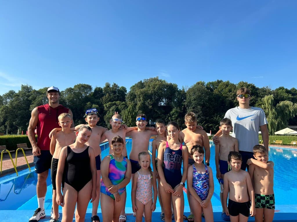 Skupina detí a trénerov pri vonkajšom bazéne